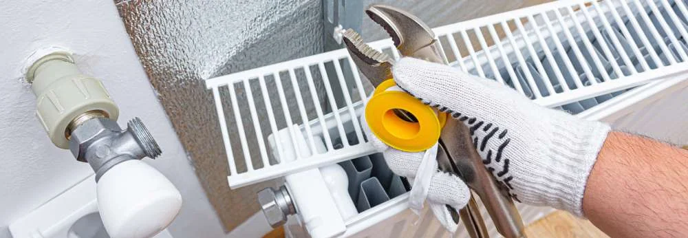 Eine Person montiert einen Heizkörper mit Zange und Dichtungsband.